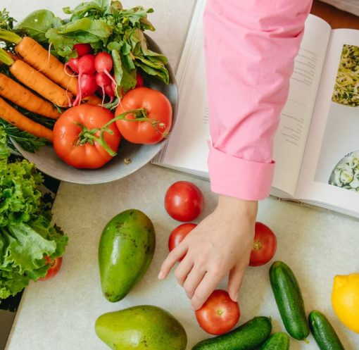 Top view of fresh vegetables and hands arranging them with a recipe book, promoting healthy eating.