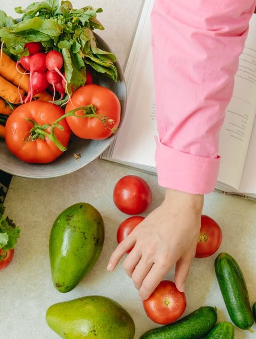 Top view of fresh vegetables and hands arranging them with a recipe book, promoting healthy eating.