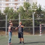 Full body cheerful father playing with football ball and mother giving piggyback ride to cute son while walking together on sports ground